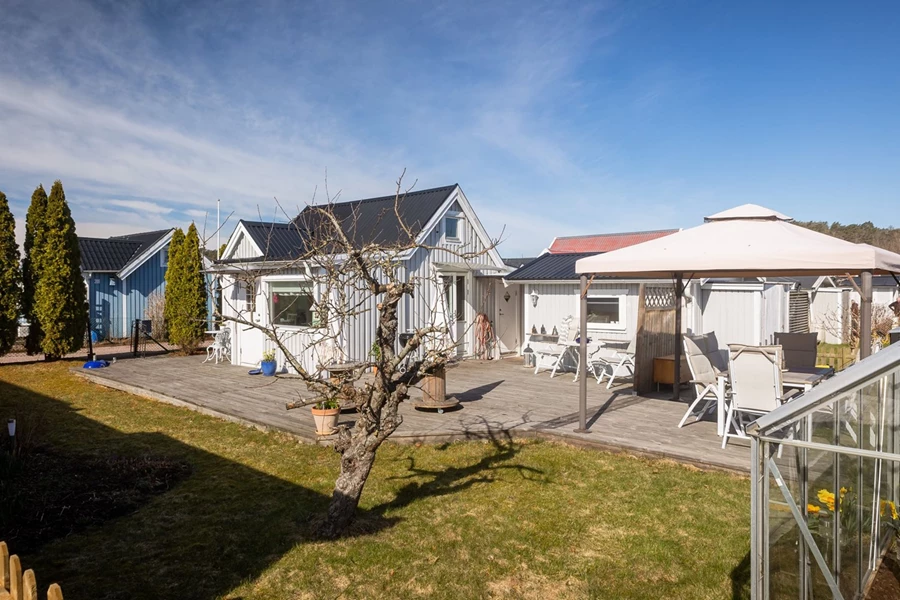 Vy inifrån trädgården mot stugan och uteplatsen