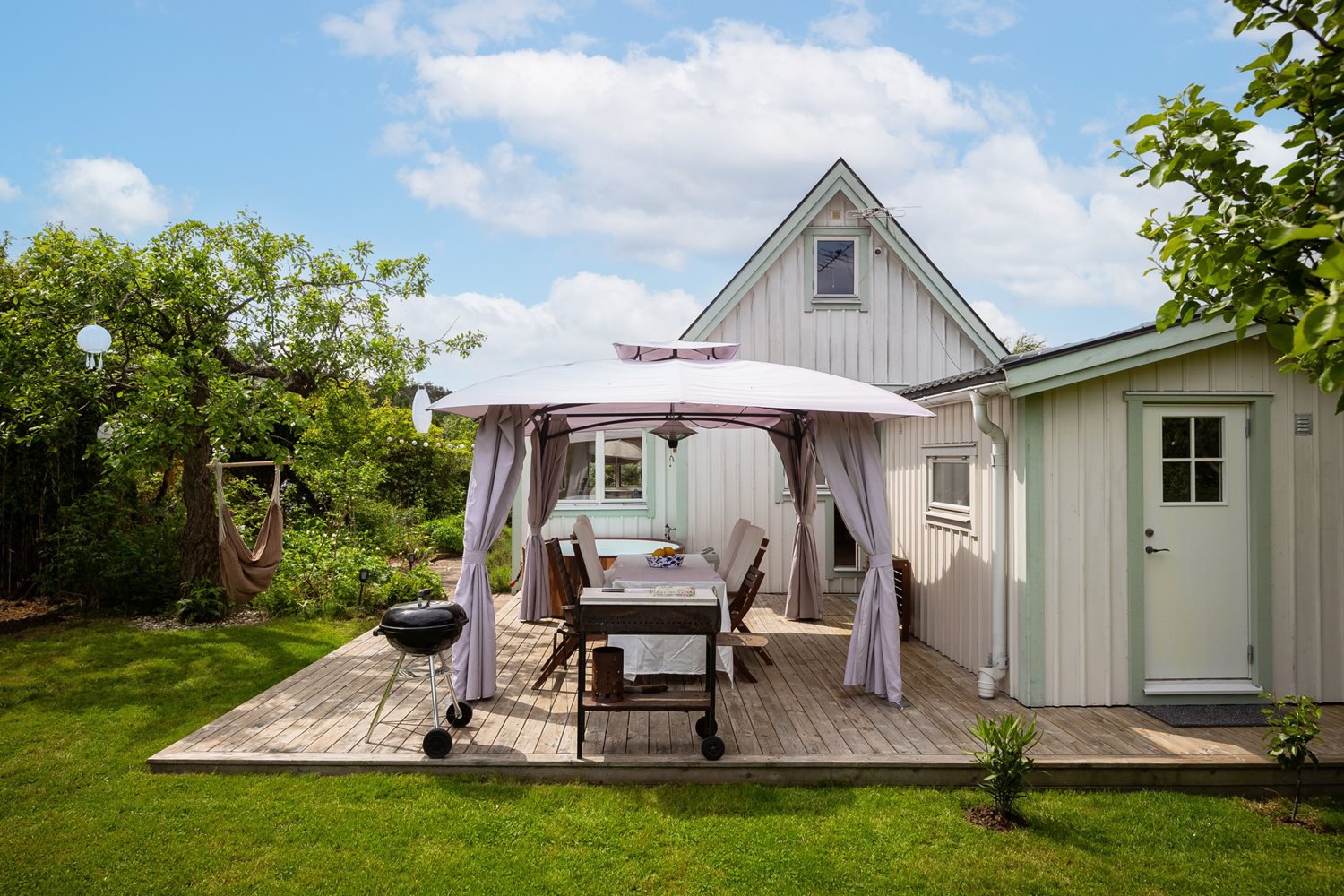 Vy inifrån trädgård mot pergola och stuga