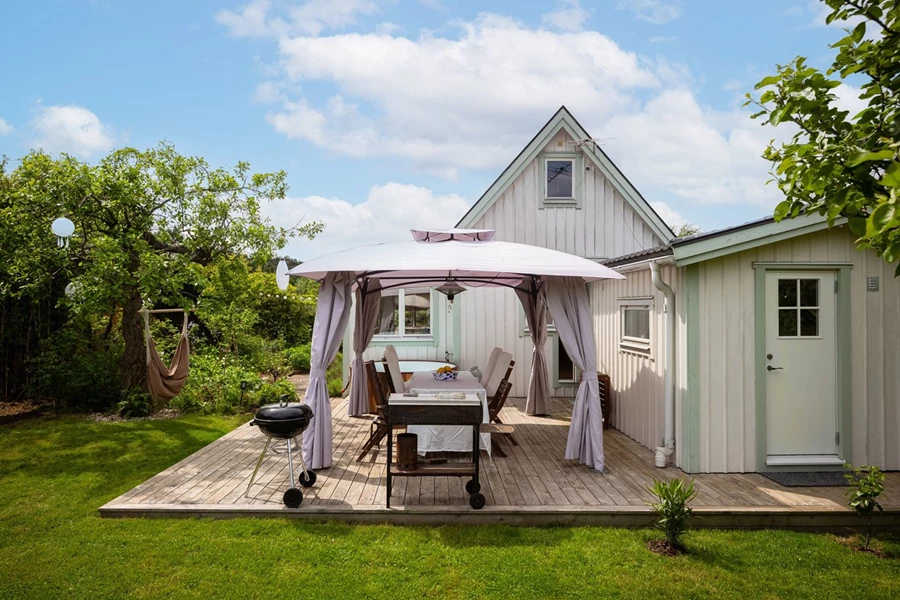 Vy inifrån trädgård mot pergola och stuga